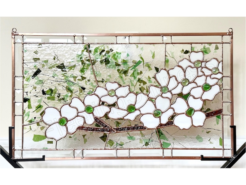 May include: A rectangular stained glass panel featuring white dogwood flowers with green glass centers on a brown branch. The background consists of clear textured glass with scattered green glass fragments, all encased in a copper metal frame.