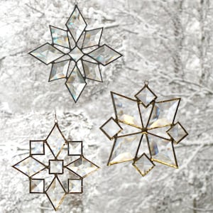 May include: Three iridescent glass snowflake ornaments with a gold wire hanger. The snowflakes are different sizes and have a geometric design.