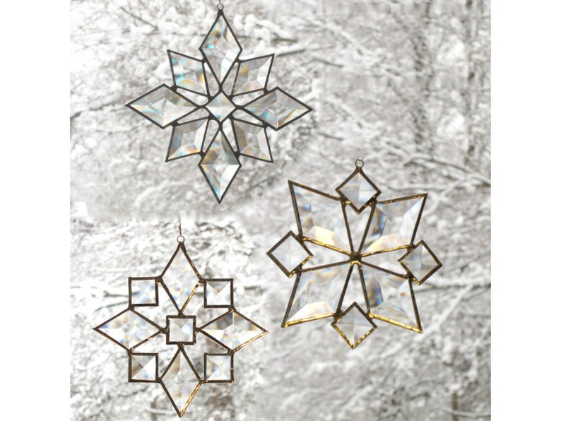 May include: Three iridescent glass snowflake ornaments with a gold wire hanger. The snowflakes are different sizes and have a geometric design.