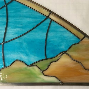 May include: A stained glass window depicting a blue sky with a horizon of brown and green hills.