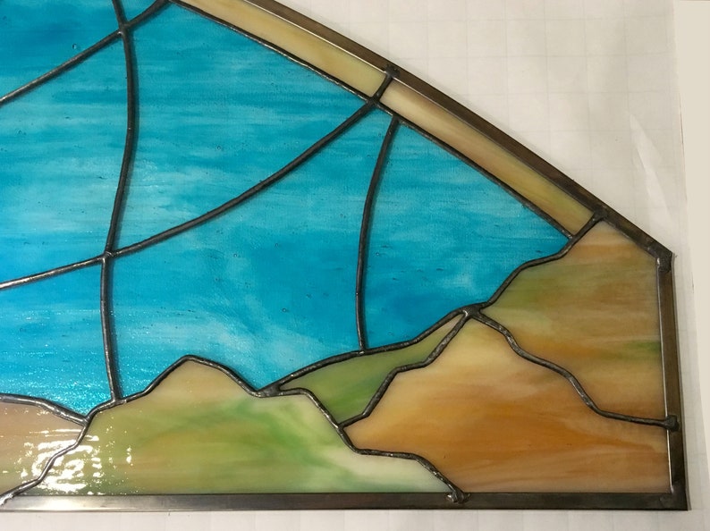 May include: A stained glass window depicting a blue sky with a horizon of brown and green hills.