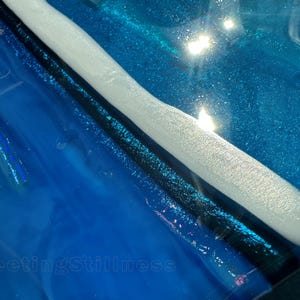 May include: A glossy blue resin surface featuring a prominent white curved ridge and a dark black line. The number 249 is printed in the top left corner, and the text FleetingStillness is visible in the bottom left area of the blue background.
