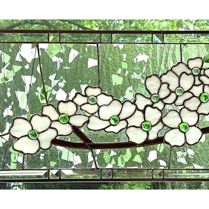 May include: A rectangular stained glass panel featuring white dogwood flowers with bright green glass centers. The flowers are arranged on a dark brown branch against a background of clear, textured glass with scattered green glass shards.