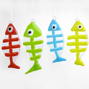 K&ouml;nnte beinhalten: Vier gl&auml;serne Fisch-Ornamente, die an einer wei&szlig;en Schnur h&auml;ngen. Die Fische sind transparent mit bemalten Skeletten. Die Fische sind rot, gr&uuml;n, blau und gelb.