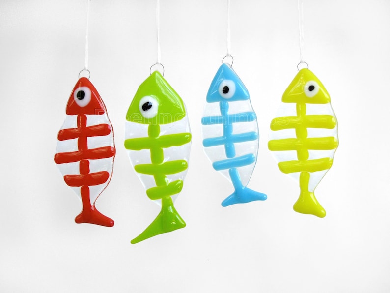 K&ouml;nnte beinhalten: Vier gl&auml;serne Fisch-Ornamente, die an einer wei&szlig;en Schnur h&auml;ngen. Die Fische sind transparent mit bemalten Skeletten. Die Fische sind rot, gr&uuml;n, blau und gelb.