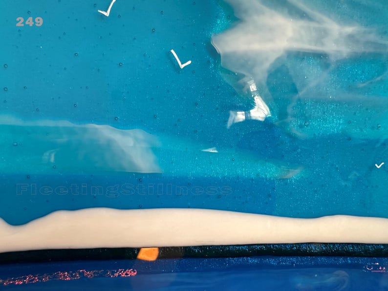 May include: A fused glass art piece featuring a vibrant blue sky with white bird silhouettes and wispy white clouds. The lower section displays a solid white horizontal band above a dark blue base. The text 249 and FleetingStillness are visible.