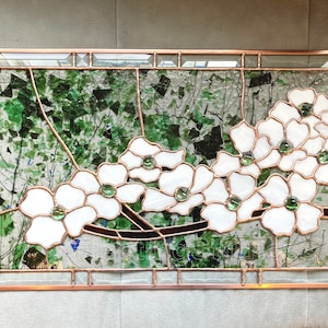 May include: A rectangular stained glass panel featuring white dogwood flowers with green glass centers, set against a background of clear glass with scattered green glass shards and dark brown branches, all encased in a copper metal frame.