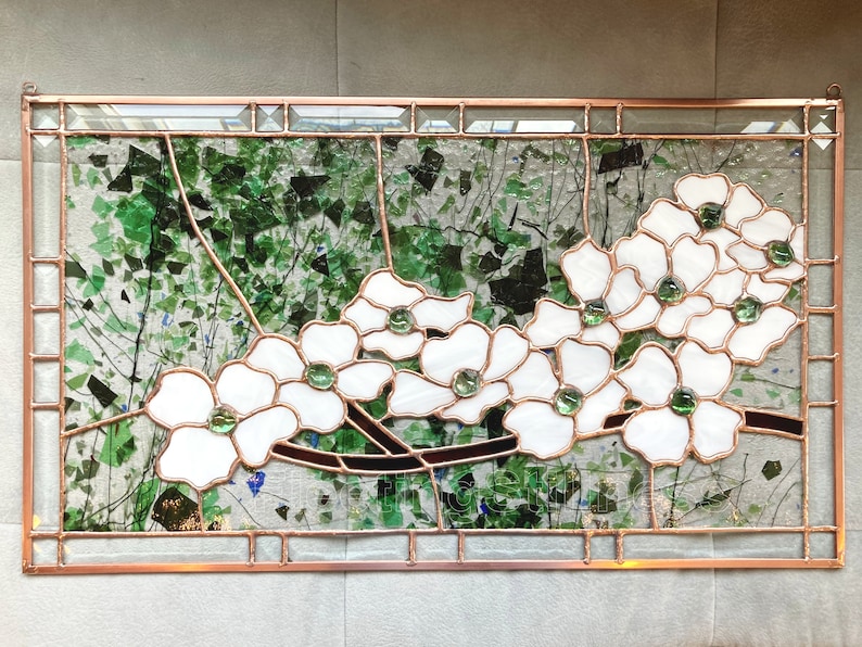 May include: A rectangular stained glass panel featuring white dogwood flowers with green glass centers, set against a background of clear glass with scattered green glass shards and dark brown branches, all encased in a copper metal frame.