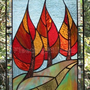 May include: Stained glass window depicting three stylized trees with red, orange, and yellow leaves. The trees are set against a blue sky with a winding path leading to the base of the trees.