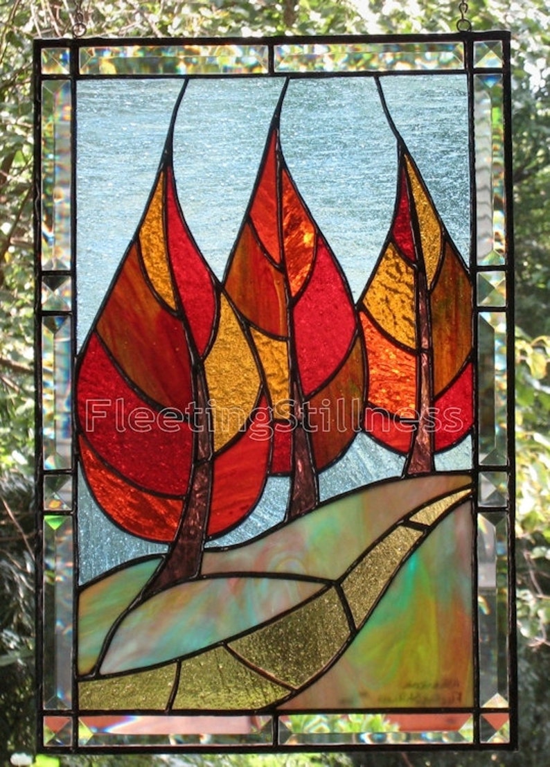 May include: Stained glass window depicting three stylized trees with red, orange, and yellow leaves. The trees are set against a blue sky with a winding path leading to the base of the trees.