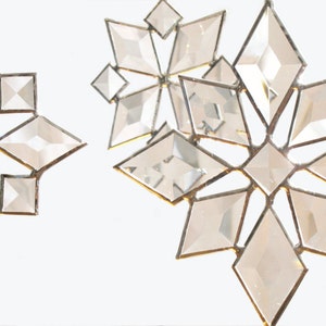 May include: Three clear glass snowflake ornaments with silver metal framing. The snowflakes are hanging from a white background.