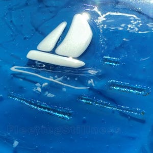 May include: A glossy blue resin art piece featuring a white sailboat silhouette with a shimmering finish. The surface displays the number 248 in the top left corner and the text FleetingStillness at the bottom, accented by blue glitter streaks.