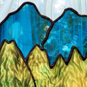 May include: A stained glass window depicting a mountain range with blue peaks and green valleys. The glass is textured and has a light, airy feel.