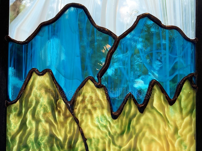 May include: A stained glass window depicting a mountain range with blue peaks and green valleys. The glass is textured and has a light, airy feel.
