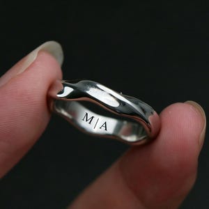 May include: A silver ring with a textured, wavy design. The ring has the initials "M|A" engraved on the inside. The ring is held up against a dark background.