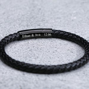 Puede incluir: Pulsera de cuero negro con cierre de metal negro. La pulsera est&aacute; grabada con el texto "Ethan & Ava 12.06".