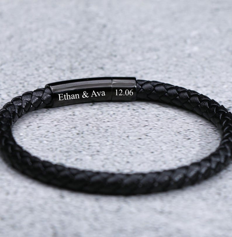Puede incluir: Pulsera de cuero negro con cierre de metal negro. La pulsera est&aacute; grabada con el texto "Ethan & Ava 12.06".