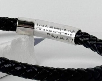 May include: Black braided leather bracelet with a silver clasp. The clasp is engraved with the text "I can do all things through Christ who strengthens me. Philippians 4:13". The bracelet is a religious accessory.