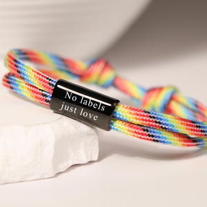 May include: A rainbow colored rope bracelet with a black metal tag that reads "No labels just love".
