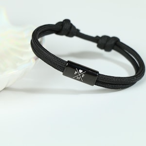May include: Black adjustable bracelet with a black metal charm engraved with "P & F" and a heart symbol. The charm also has the number "23" engraved on it.