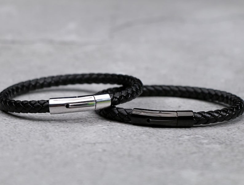 Puede incluir: Dos pulseras de cuero negro con cierres de metal plateado y negro.
