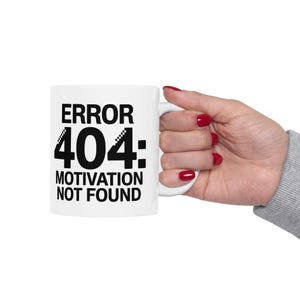 May include: White ceramic mug featuring the text "ERROR 404: MOTIVATION NOT FOUND" in black. The mug is held by a hand with red nail polish.
