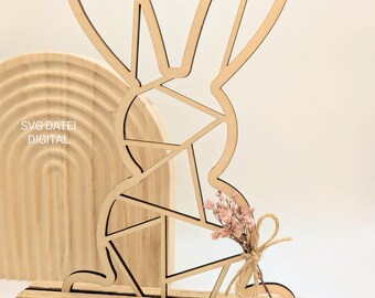 May include: A wooden geometric bunny cutout with a stand. The bunny is holding a small bouquet of dried flowers tied with twine. The bunny is a light brown color and the stand is a darker brown.