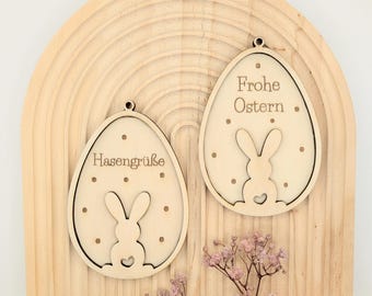 May include: Two wooden Easter egg ornaments with bunny silhouettes and engraved text. The left ornament says "Hasengrüße" and the right ornament says "Frohe Ostern".