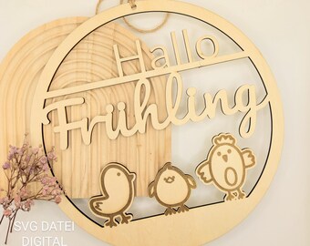 May include: A wooden round sign with the text "Hallo Frühling" in a decorative font. The sign is decorated with three small, stylized chicks.
