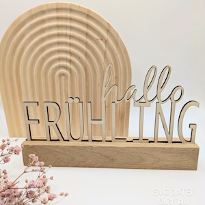 Könnte beinhalten: Holzschilder mit dem Text "hallo FRÜHLING" in einer dekorativen Schriftart. Das Schild steht auf einem Holzsockel und befindet sich vor einem Holzregenbogen.