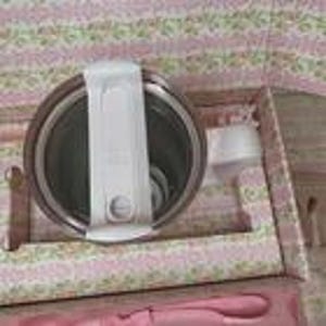 May include: A stainless steel insulated food container with a white lid and handle, presented in a floral-patterned box. The container is designed to keep food warm or cold. A pink spoon is also visible.