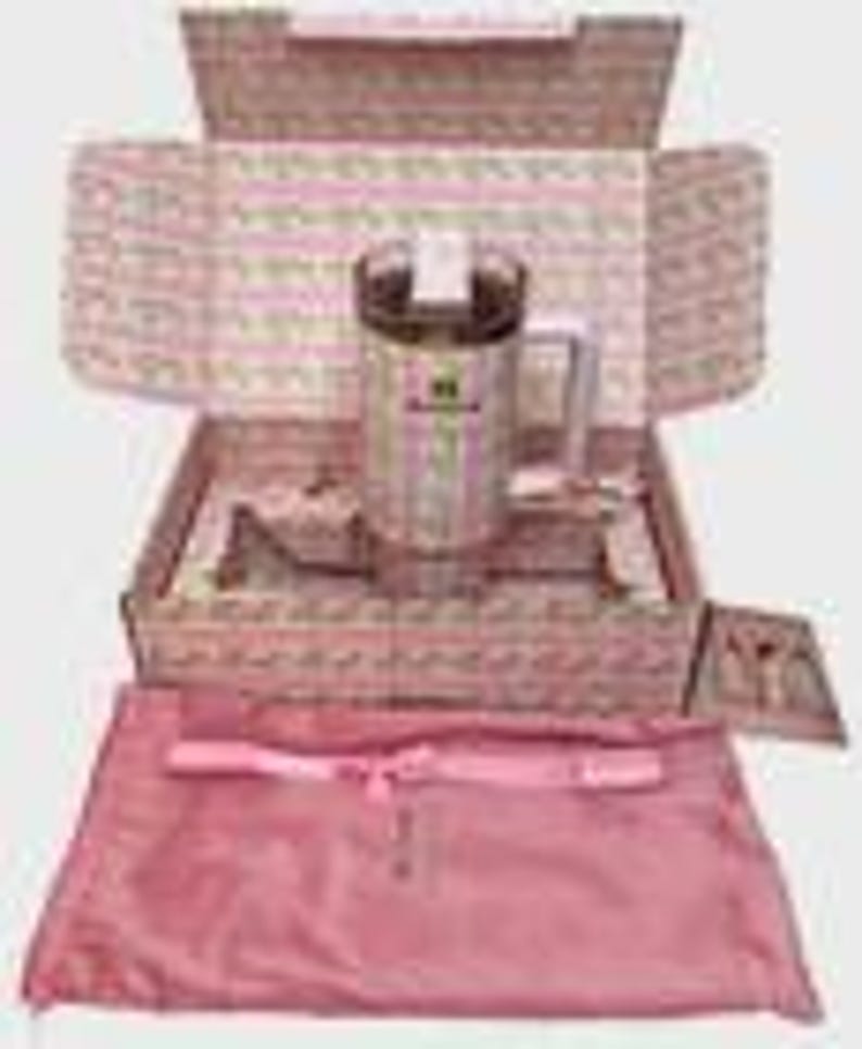 May include: A stainless steel travel mug with a handle and a clear lid, presented in a decorative box with a pink and white floral pattern. The box contains a pink satin bag and a small card. The mug has a green and white label.