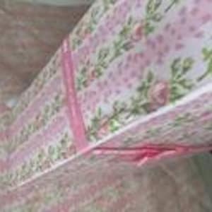 May include: A floral patterned gift box with a pink and white design. The box features a repeating pattern of small pink roses and green leaves. Pink ribbon is tied around the box. The box is open, revealing the inside.