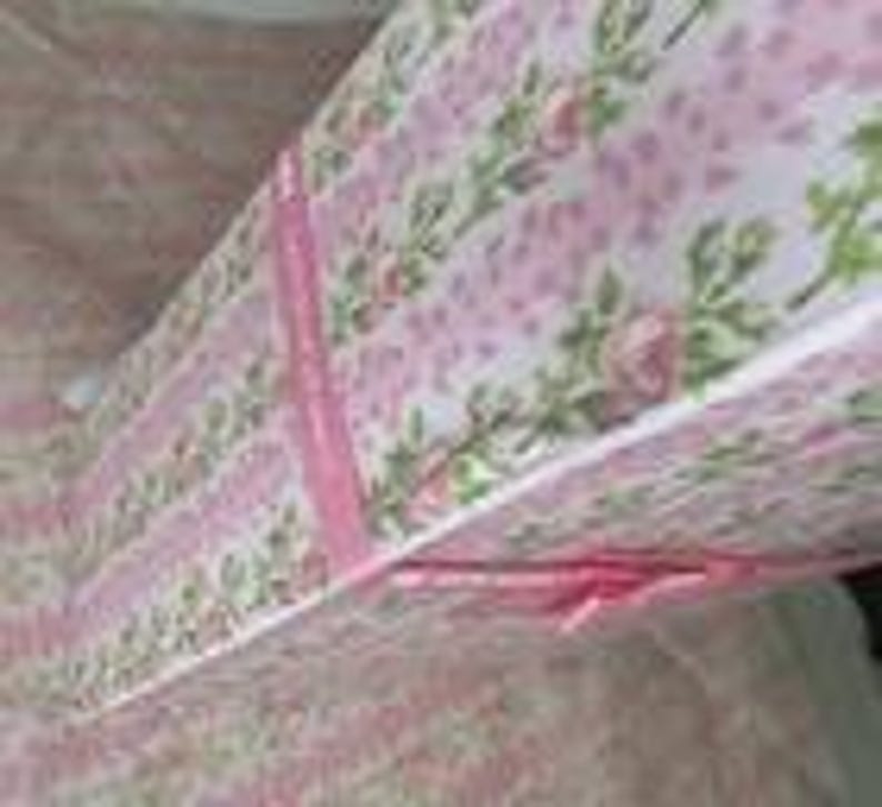 May include: A floral patterned gift box with a pink and white design. The box features a repeating pattern of small pink roses and green leaves. Pink ribbon is tied around the box. The box is open, revealing the inside.