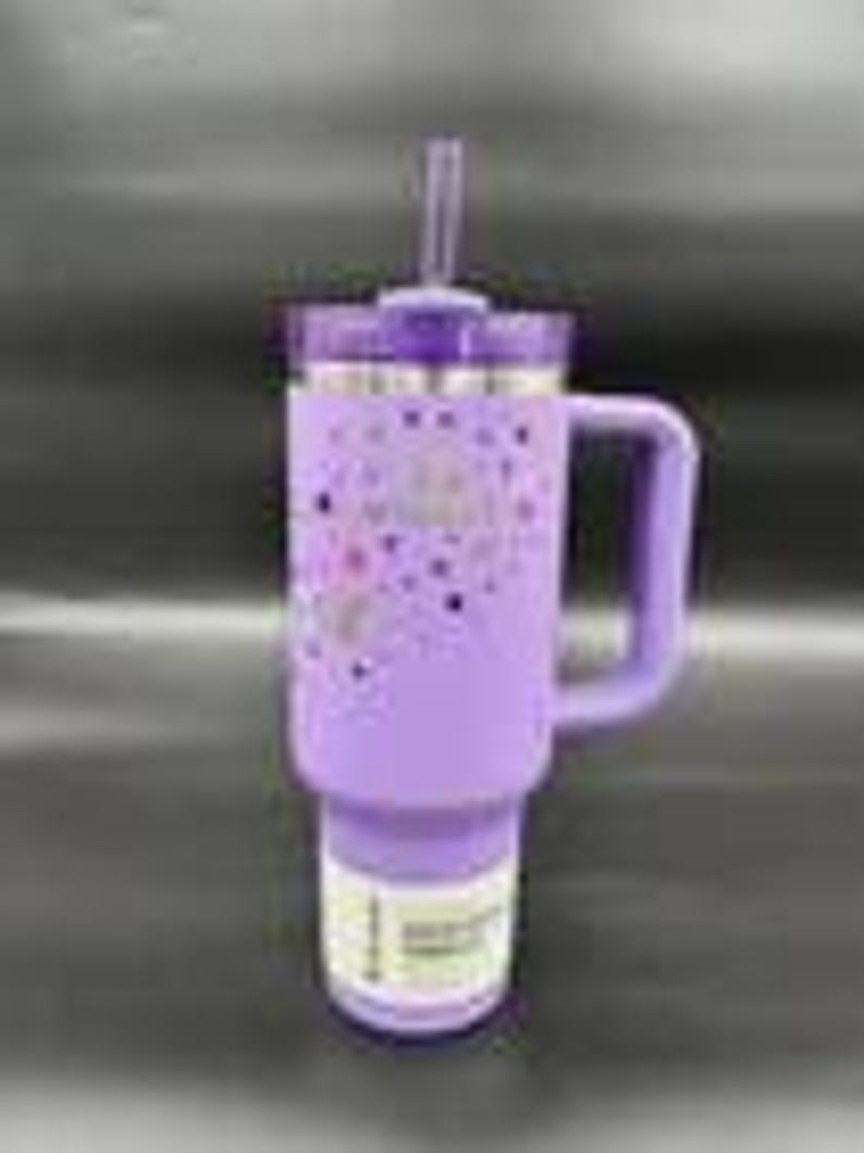 Pu&ograve; includere: Un bicchiere termico lavanda con manico e cannuccia. Il bicchiere ha un coperchio viola e un bordo argentato. Il corpo del bicchiere &egrave; decorato con un motivo di cuori e stelle rosa e viola. Il bicchiere &egrave; progettato per bevande fredde.