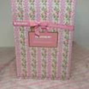 May include: A rectangular gift box wrapped in pink paper with vertical stripes and a floral pattern. A pink ribbon is tied around the box, and a rectangular label is affixed to the front. The text on the label reads "The Wedding Box".