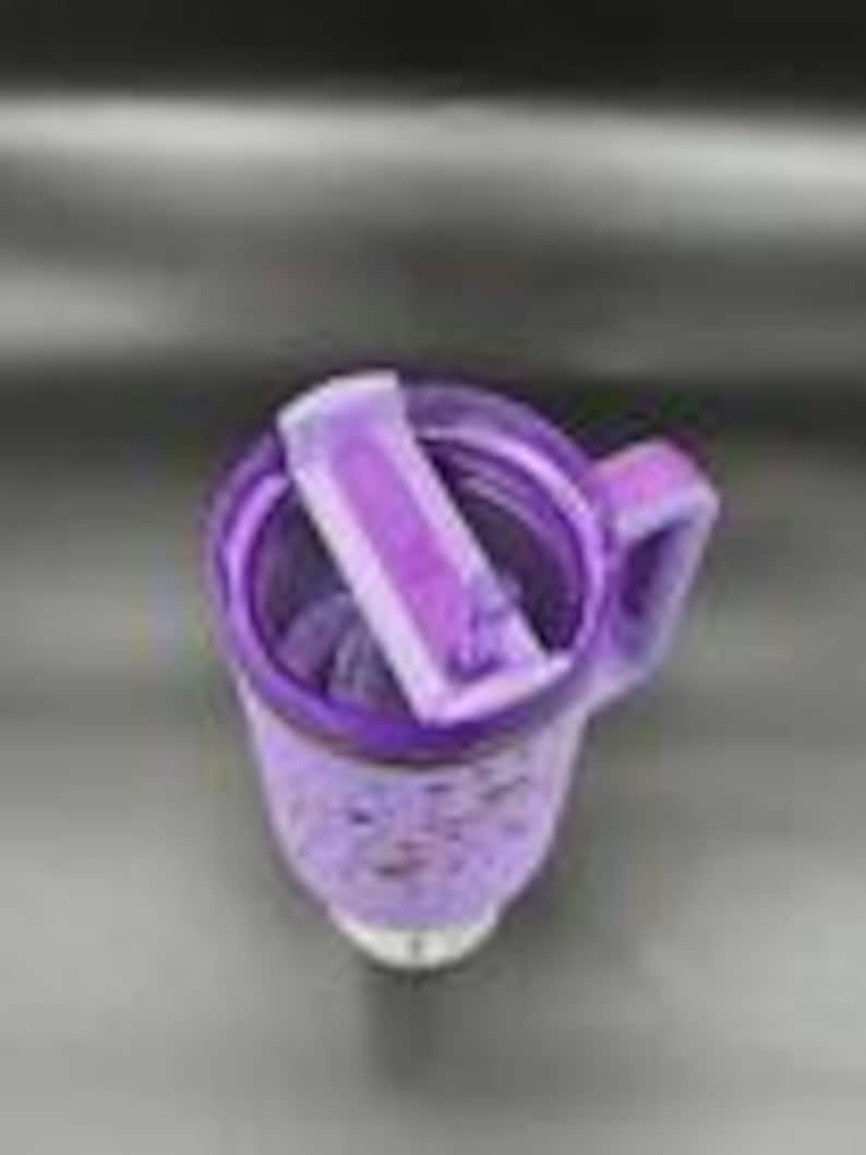 Pu&ograve; includere: Tazza da viaggio isolante viola con manico e coperchio ribaltabile. La tazza ha un design maculato e una base bianca. Il coperchio &egrave; aperto, rivelando l'interno. La tazza &egrave; progettata per mantenere le bevande calde o fredde.
