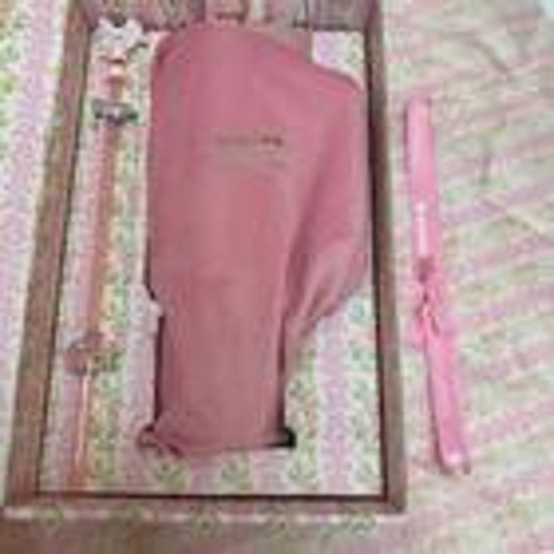 May include: A pink and gold wand and a pink knife are displayed in a wooden box. The wand has a star-shaped top and a clear handle. The knife is pink with a white handle. The box is lined with a floral patterned fabric.