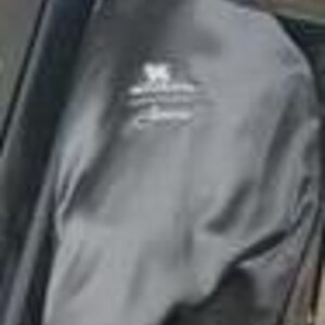 Puede incluir: Una funda para ropa de color negro con un logotipo bordado en blanco en la parte frontal. La funda est&aacute; hecha de una tela oscura y lisa, y se encuentra parcialmente abierta, dejando ver una parte del forro interior. El logo incluye un gr&aacute;fico.