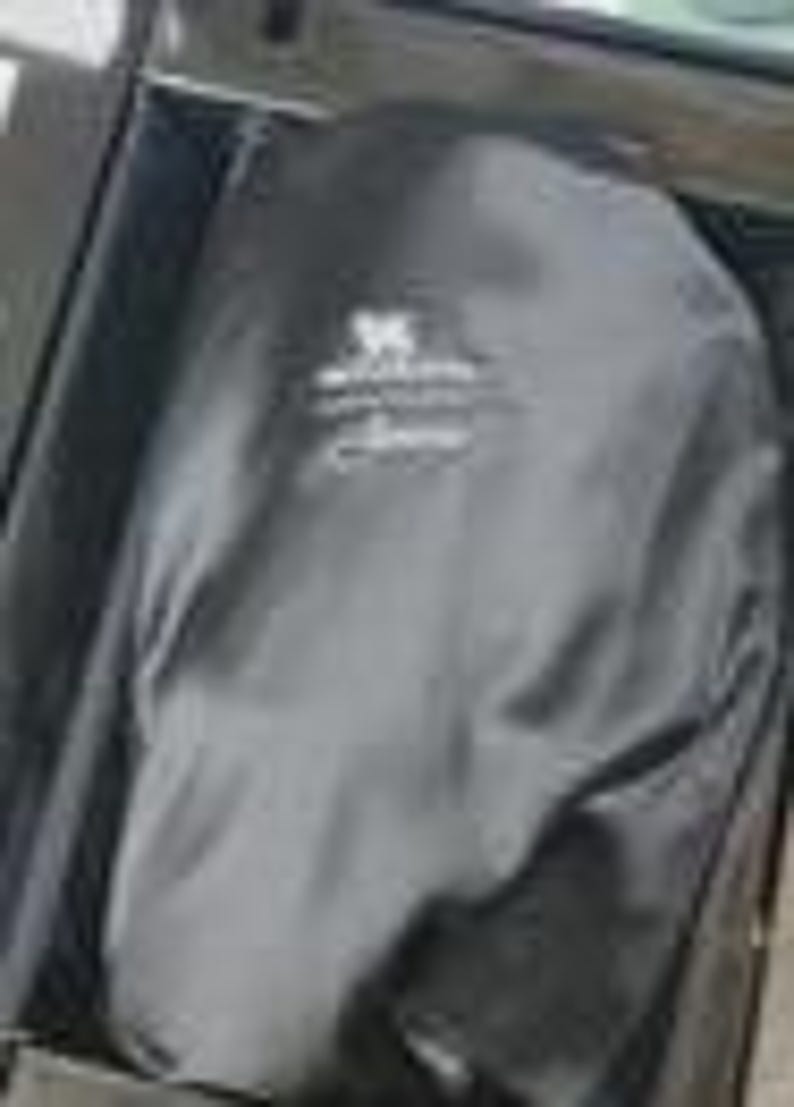 Puede incluir: Una funda para ropa de color negro con un logotipo bordado en blanco en la parte frontal. La funda est&aacute; hecha de una tela oscura y lisa, y se encuentra parcialmente abierta, dejando ver una parte del forro interior. El logo incluye un gr&aacute;fico.