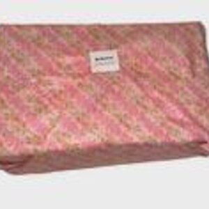 May include: A rectangular package wrapped in pink floral patterned paper with diagonal stripes. A small white label is affixed to the top. The package is likely a gift or a product ready for shipping.