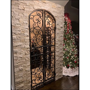 May include: A black wrought iron gate with a decorative scroll design, leading to a wine cellar. The gate is set into a wall of stacked stone tiles.