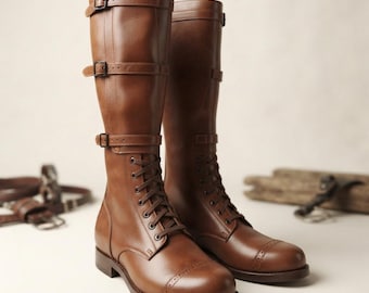 Könnte beinhalten: Ein Paar kniehohe braune Lederstiefel mit abgerundeter Zehenpartie und dekorativen Brogue-Details, einer Schnürung an der Vorderseite sowie drei horizontalen Riemen mit Metallschnallen an der Außenseite des Schafts.