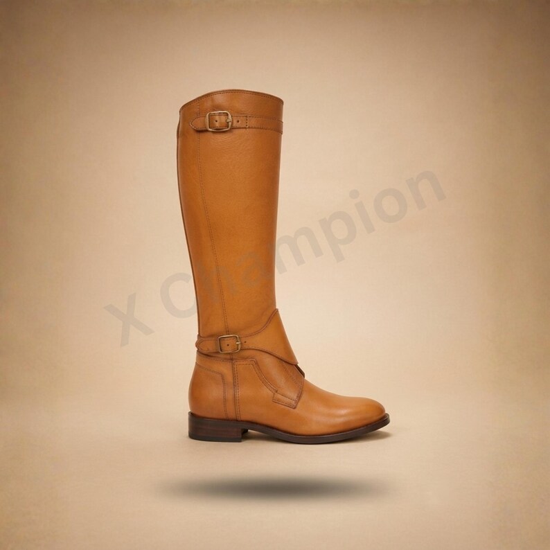 K&ouml;nnte beinhalten: Ein kniehoher Stiefel in Hellbraun aus glattem Leder mit niedrigem Blockabsatz und zwei verstellbaren Riemen mit messingfarbenen Metallschnallen am Kn&ouml;chel und am Schaftabschluss. Der Text x champion ist an der Seite zu sehen.