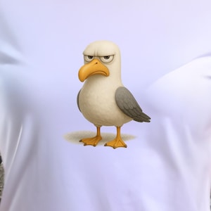 Könnte beinhalten: Weißes T-Shirt mit einem Cartoon-Möwen-Design. Die Möwe hat einen wütenden Gesichtsausdruck, einen gelben Schnabel und Füße, graue Flügel und einen weißen Körper. Das T-Shirt ist ein klassischer Rundhalsausschnitt.