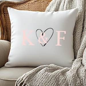 Könnte beinhalten: Weißes quadratisches Kissen mit den Buchstaben "K & F" in Rosa und einem schwarzen Herzdesign. Das Kissen liegt auf einem Vintage-Sessel mit einer beigen Decke.