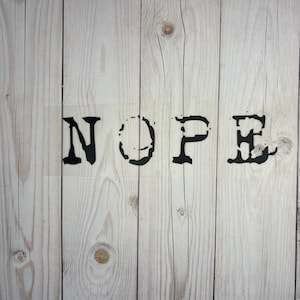 Könnte beinhalten: Das Wort "NOPE" ist in schwarzen Buchstaben auf einem weißen Holzgrund gedruckt.