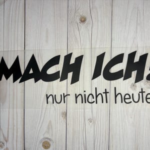 Könnte beinhalten: Schwarz-weißer Vinyl-Aufkleber mit dem Text "MACH ICH! nur nicht heute..." auf einem Holzgrund.