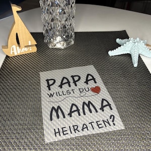 Könnte beinhalten: Eine weiße Karte mit schwarzem Text, der "Papa willst du Mama heiraten?" lautet, mit einem roten Herzen über dem Wort "Mama".
