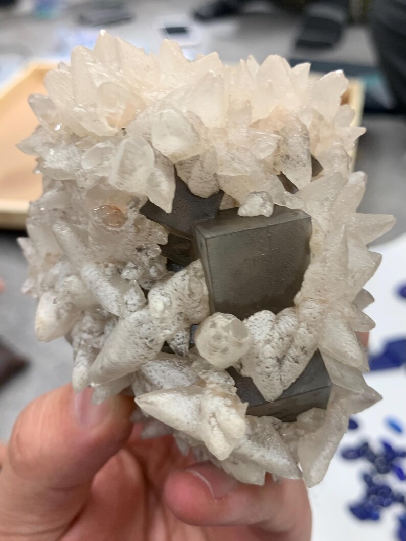 May include: A cluster of clear, crystalline formations with a spiky appearance, surrounding several dark gray, cube-shaped structures. The overall color palette is neutral, with shades of white, gray, and clear.